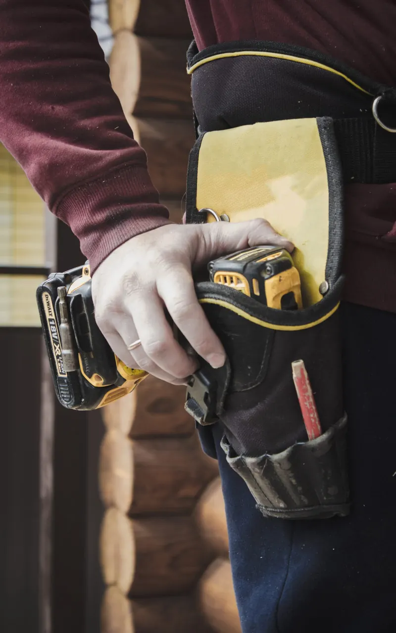 Close-up of a worker drawing a cordless drill from a tool belt holster