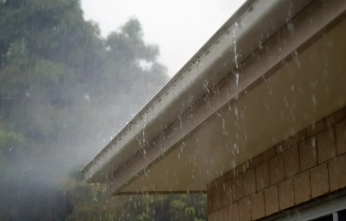 Rainwater pouring over the front edge of a white gutter during a heavy downpour