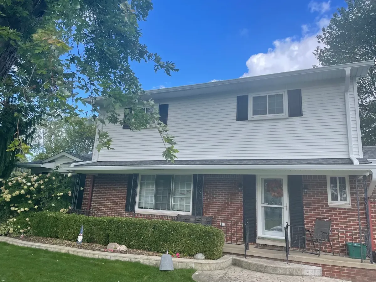 Two-story brick and vinyl-sided home with white seamless gutters along both rooflines and white downspouts at the corners